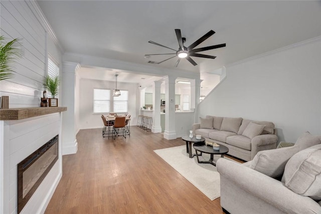 living room featuring decorative columns, hardwood / wood-style flooring, ceiling fan, and ornamental molding