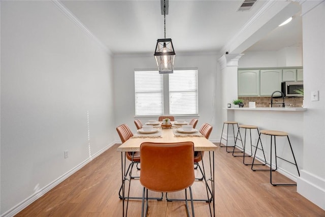 dining space featuring light hardwood / wood-style floors, sink, crown molding, and ornate columns