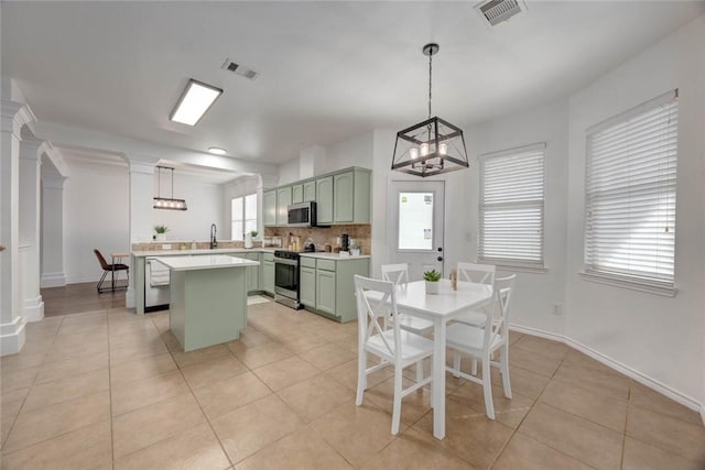 kitchen with pendant lighting, backsplash, light tile patterned flooring, green cabinetry, and stainless steel appliances