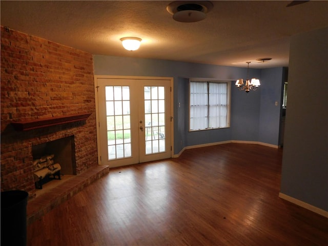 unfurnished living room featuring a textured ceiling, a chandelier, dark hardwood / wood-style flooring, a brick fireplace, and french doors