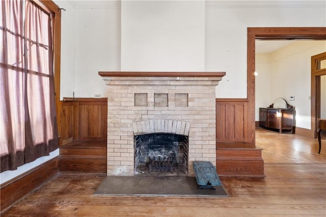 living area with a wainscoted wall, wood walls, a fireplace, and wood finished floors