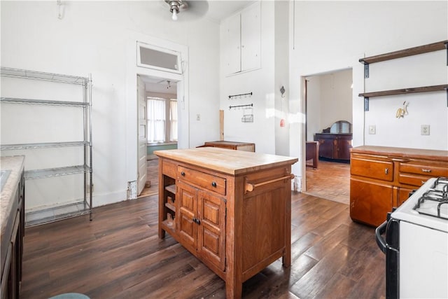 kitchen with white range with gas cooktop, brown cabinets, open shelves, dark wood-style floors, and butcher block counters
