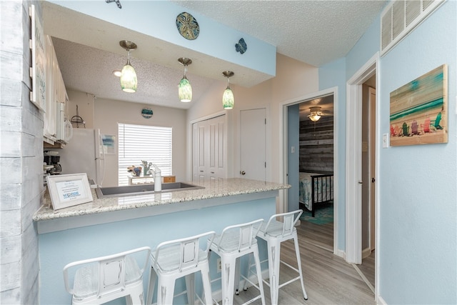 kitchen featuring kitchen peninsula, hanging light fixtures, a textured ceiling, light hardwood / wood-style flooring, and white appliances