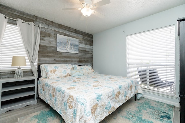 bedroom featuring hardwood / wood-style floors, ceiling fan, a textured ceiling, and wood walls