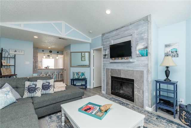 living room featuring a high end fireplace, wood-type flooring, a textured ceiling, and vaulted ceiling