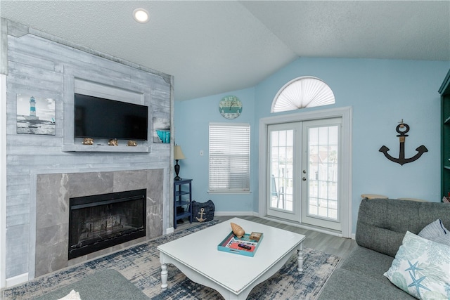 living room with french doors, a fireplace, a textured ceiling, vaulted ceiling, and hardwood / wood-style flooring