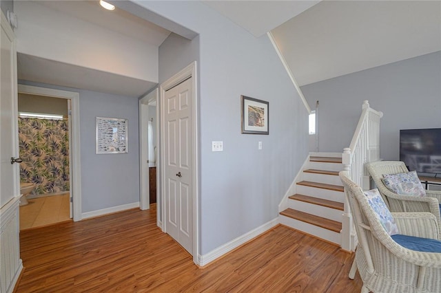 hall featuring stairway, baseboards, lofted ceiling, and light wood finished floors