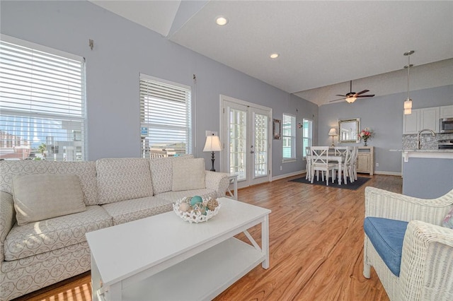 living area featuring baseboards, recessed lighting, vaulted ceiling, french doors, and light wood-type flooring