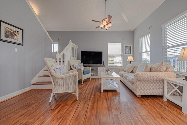 living area with lofted ceiling, a ceiling fan, light wood finished floors, baseboards, and stairs