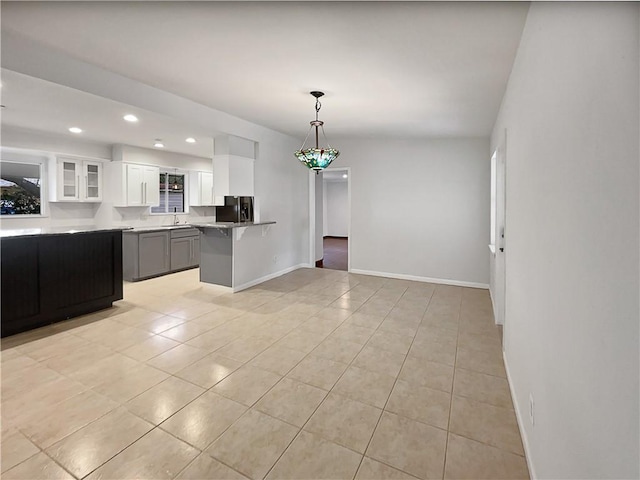 kitchen with white cabinets, a peninsula, hanging light fixtures, light countertops, and a sink