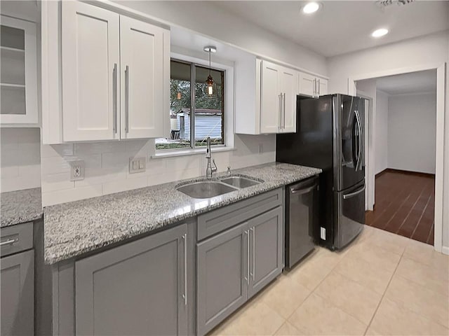 kitchen featuring dishwasher, glass insert cabinets, light stone countertops, white cabinetry, and a sink