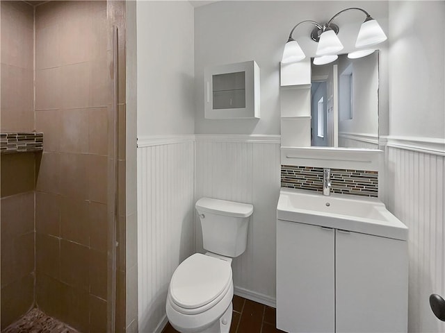 bathroom featuring toilet, vanity, a tile shower, and wainscoting