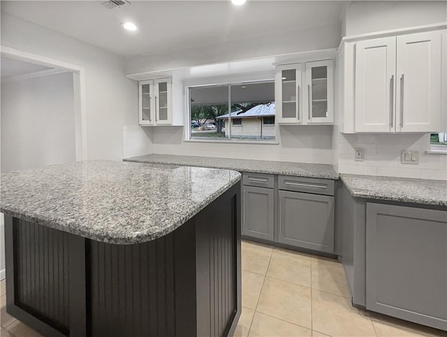 kitchen featuring light tile patterned floors, gray cabinetry, glass insert cabinets, white cabinetry, and light stone countertops