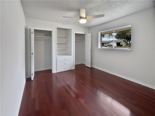 unfurnished bedroom with a textured ceiling, dark wood finished floors, and multiple closets