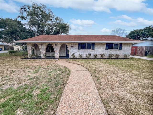 single story home with a shingled roof, a front yard, brick siding, and fence