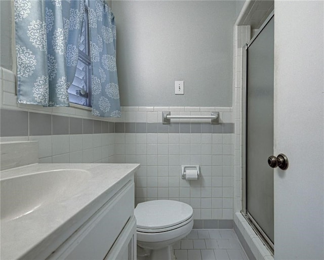 bathroom with tile walls, tile patterned floors, a shower with door, vanity, and toilet