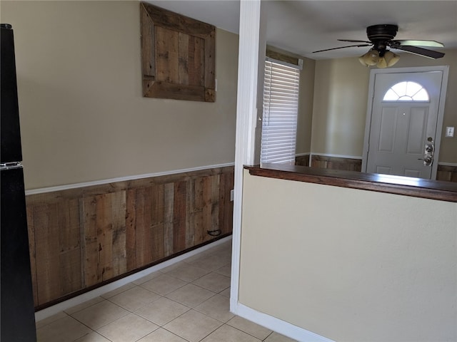 foyer with light tile patterned floors, ceiling fan, and wood walls