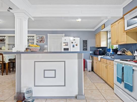 kitchen featuring light brown cabinetry, ornate columns, light tile patterned floors, ornamental molding, and white appliances