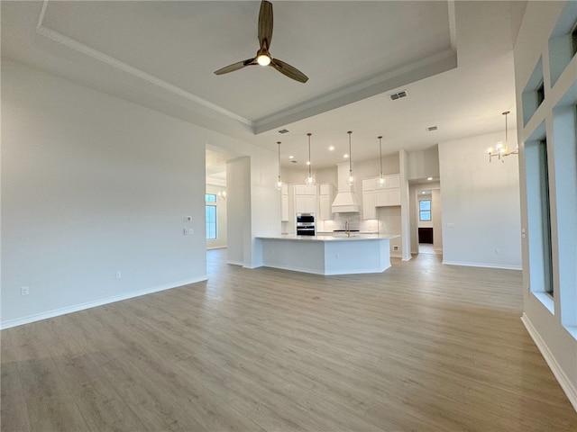 unfurnished living room featuring a raised ceiling, crown molding, and light hardwood / wood-style flooring