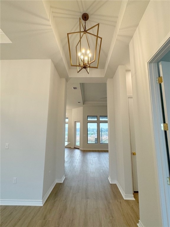 hall with a chandelier, light hardwood / wood-style floors, and a tray ceiling