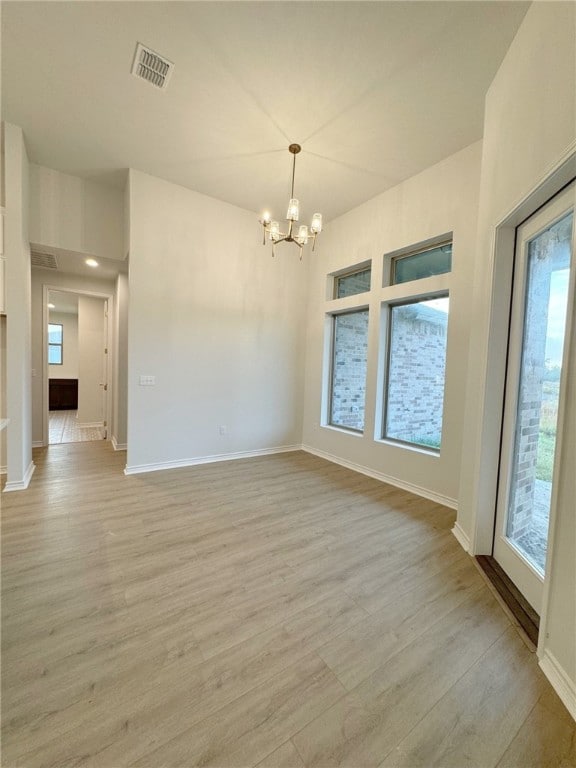 spare room featuring a chandelier and light hardwood / wood-style flooring