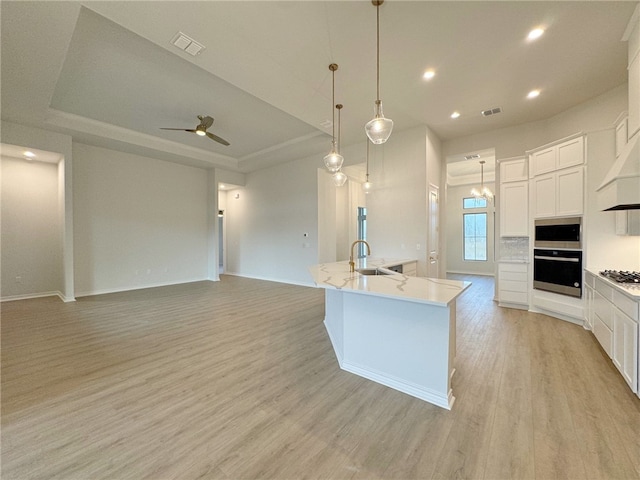 kitchen with appliances with stainless steel finishes, light wood-type flooring, a kitchen island with sink, decorative light fixtures, and white cabinets