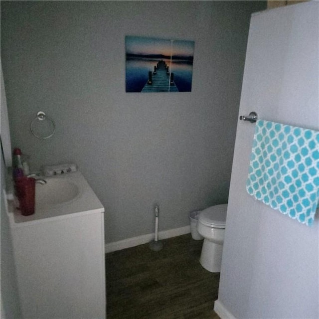 bathroom with toilet, wood finished floors, baseboards, and a sink