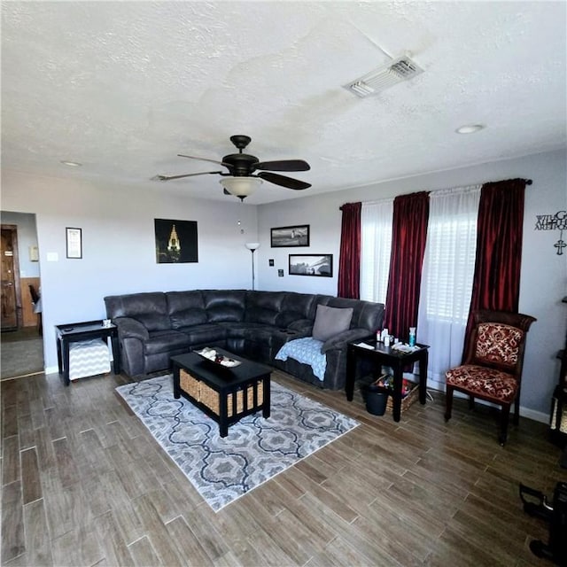 living area with a textured ceiling, a ceiling fan, visible vents, and wood finish floors