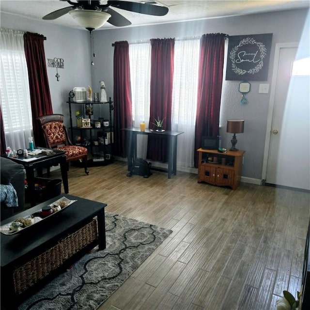 living area with a ceiling fan, baseboards, and wood finished floors