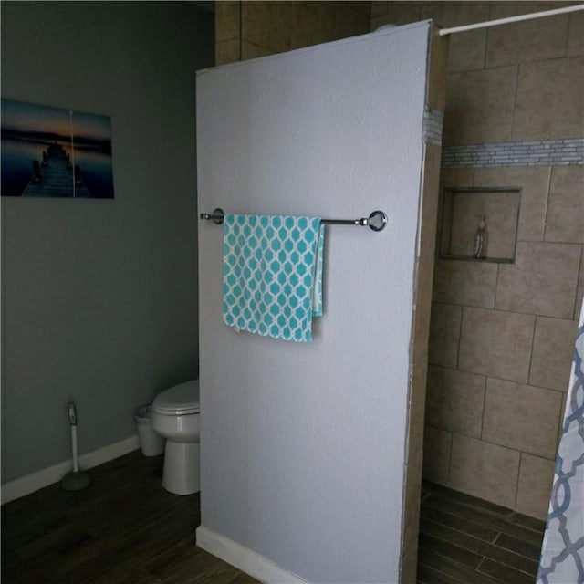 full bathroom featuring a walk in shower, toilet, baseboards, and wood finished floors