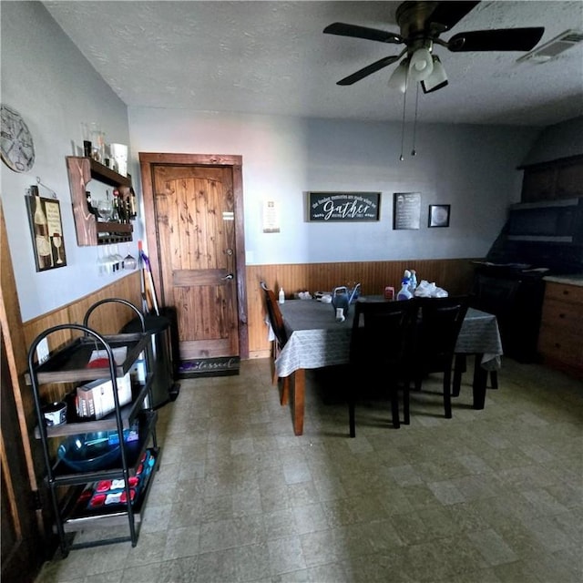 dining space with visible vents, wooden walls, wainscoting, and a textured ceiling