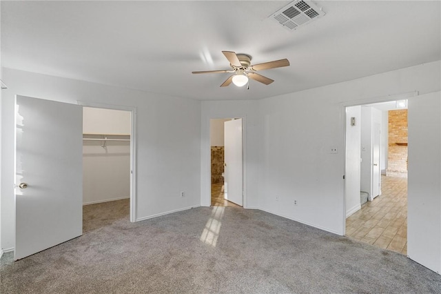 unfurnished bedroom featuring a closet, light colored carpet, a spacious closet, and ceiling fan