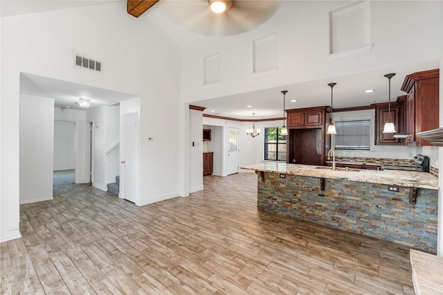 kitchen with ceiling fan with notable chandelier, beamed ceiling, decorative light fixtures, light hardwood / wood-style floors, and kitchen peninsula