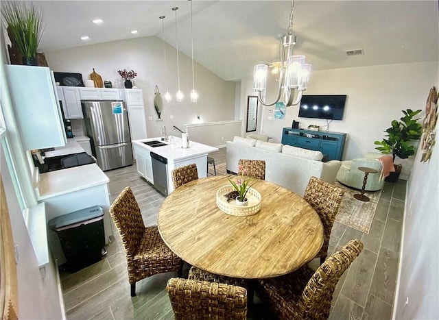 dining space featuring light wood-type flooring, an inviting chandelier, vaulted ceiling, and sink