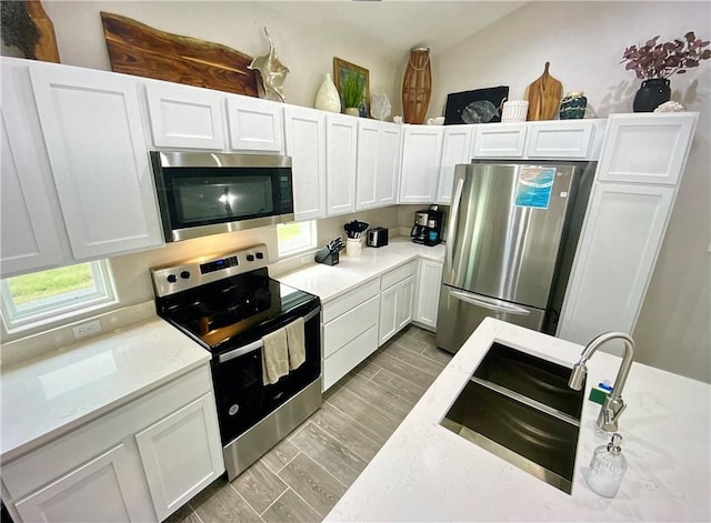 kitchen with appliances with stainless steel finishes, light wood-type flooring, white cabinetry, and sink