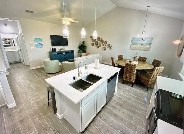 kitchen featuring stainless steel dishwasher, vaulted ceiling, sink, a center island with sink, and light hardwood / wood-style floors