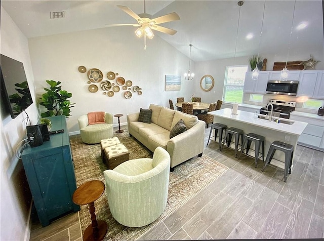 living room featuring ceiling fan with notable chandelier, light wood-type flooring, sink, and high vaulted ceiling