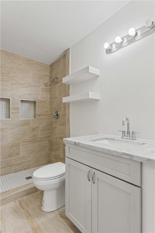 bathroom with vanity, toilet, tile patterned flooring, and a tile shower