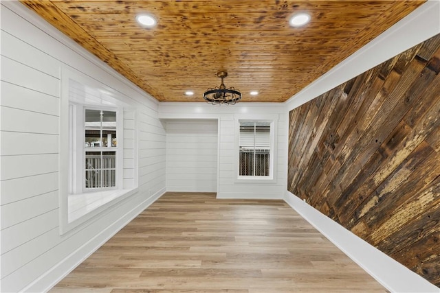 empty room with light wood-type flooring, an inviting chandelier, wood ceiling, and wood walls