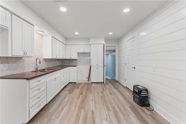 kitchen with sink, light wood-type flooring, dark stone countertops, white cabinets, and backsplash