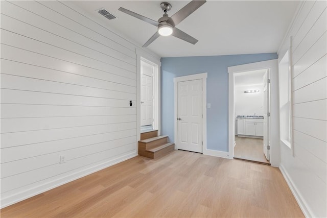 unfurnished bedroom featuring ensuite bathroom, vaulted ceiling, light hardwood / wood-style flooring, wooden walls, and ceiling fan