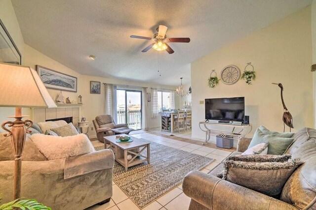 tiled living room with lofted ceiling, ceiling fan with notable chandelier, a textured ceiling, and a tile fireplace