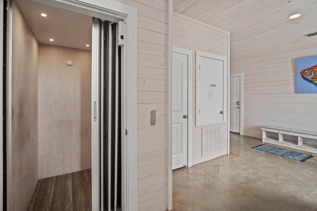 hallway with elevator, wooden walls, and concrete floors