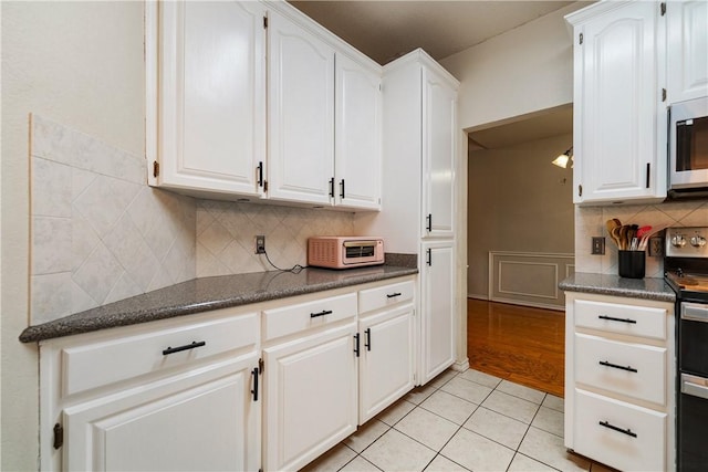 kitchen with white cabinets, a toaster, light tile patterned flooring, decorative backsplash, and appliances with stainless steel finishes