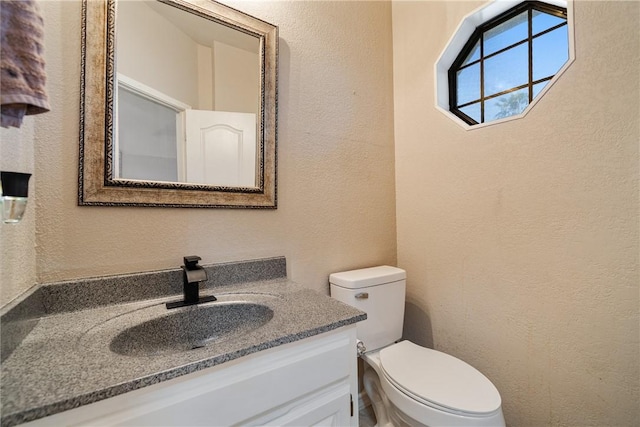 half bath featuring a textured wall, toilet, and vanity