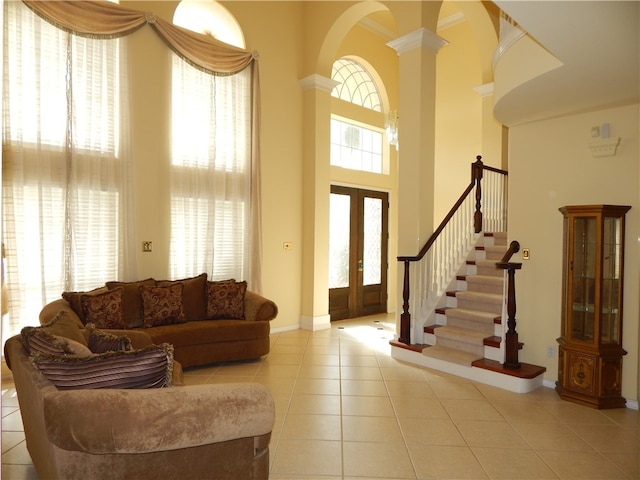 tiled living room featuring french doors, ornate columns, and a towering ceiling