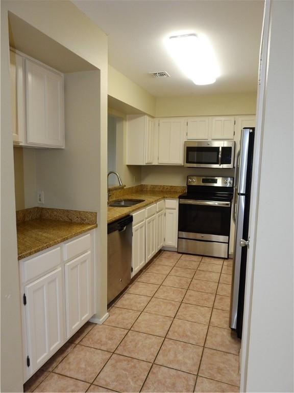 4401 River Valley Dr, Corpus Christi, TX 78410 - kitchen featuring appliances with stainless steel finishes, white cabinets, light tile patterned floors, and stone countertops