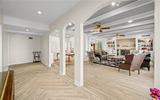 living room with beamed ceiling, a large fireplace, light hardwood / wood-style floors, and ceiling fan