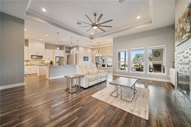 living room with ceiling fan with notable chandelier, a tray ceiling, and dark hardwood / wood-style floors