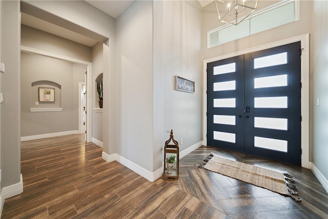 foyer entrance with a notable chandelier, dark wood-type flooring, a high ceiling, and french doors